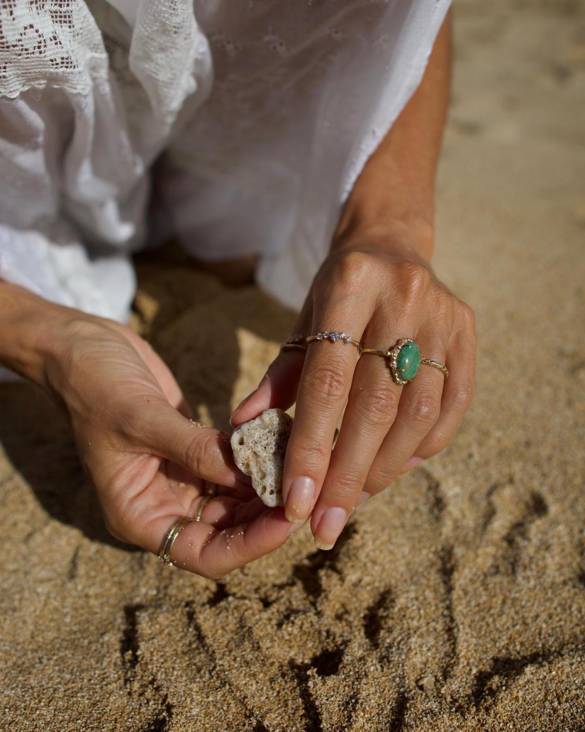 A photo of sand on the beach, with someone kneeling down and holding a piece of coral.